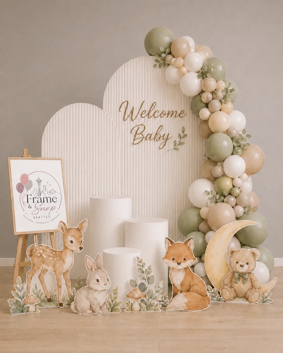 Sage and cream balloons, textured curved backdrops and woodland animal illustrations create a welcome-baby setting.